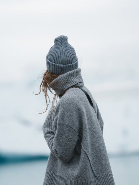 A photograph of a woman wearing a grey sweater and a beanie standing before a cold beach.